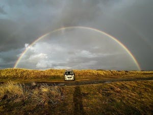 campervan in sand dunes under a rainbow