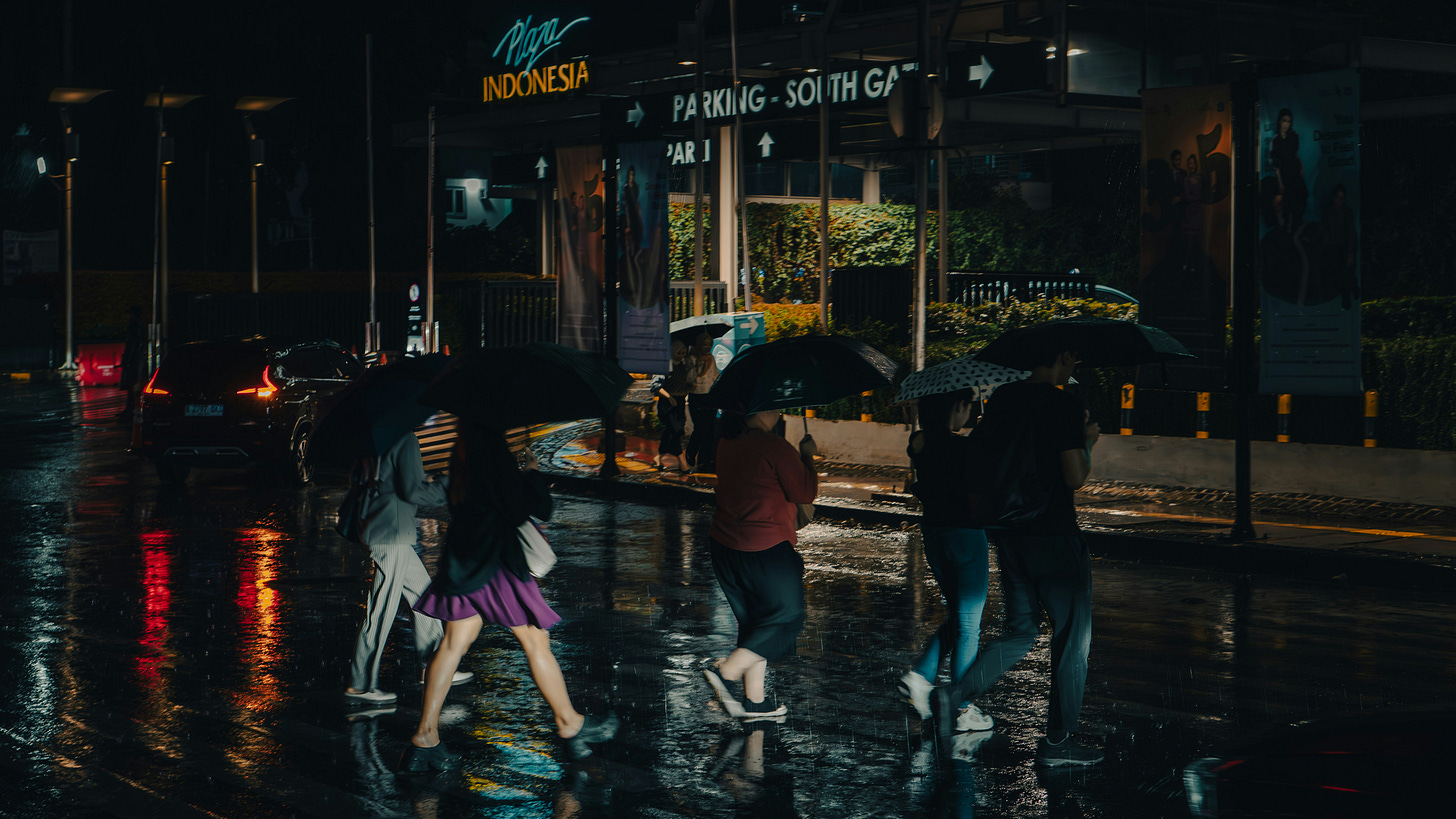 Several pedestrians crossed the road in front of Plaza Indonesia while carrying umbrellas during heavy rain