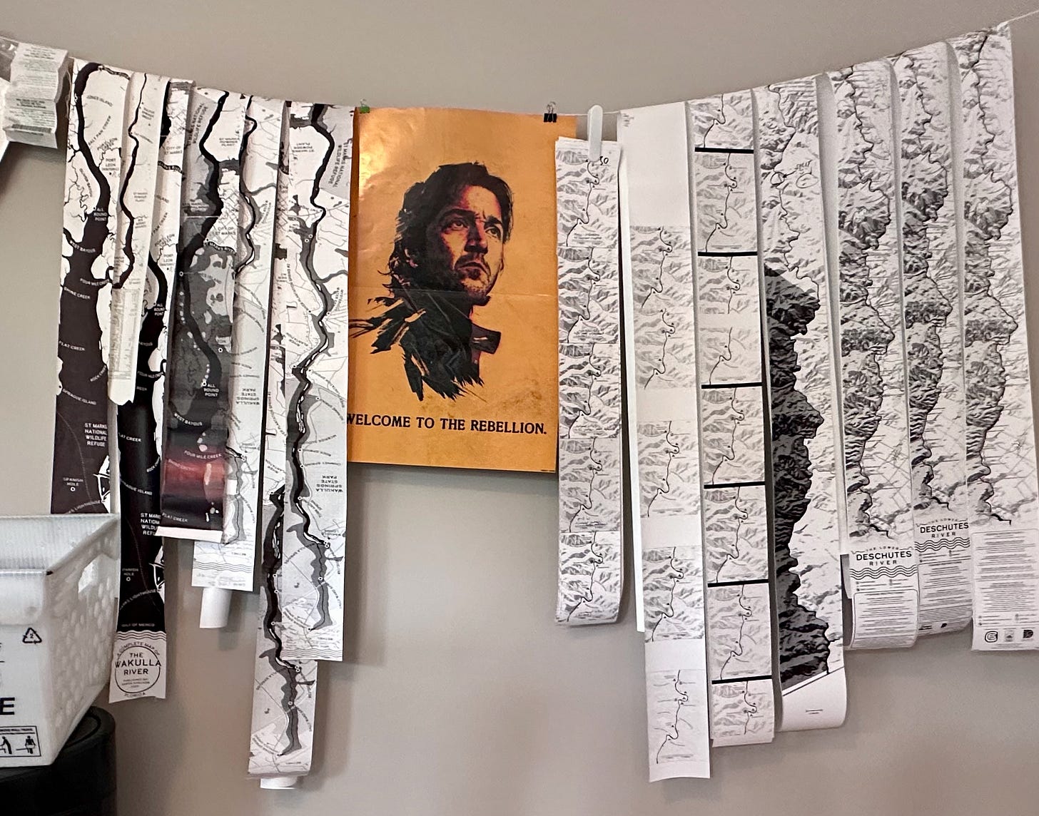 Lower Deschutes Ribbon Maps hanging from a string across a wall, with a Cassian Andor poster in the middle