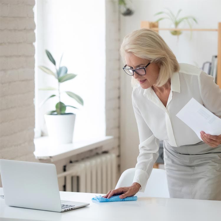 Woman cleaning desk around laptop.