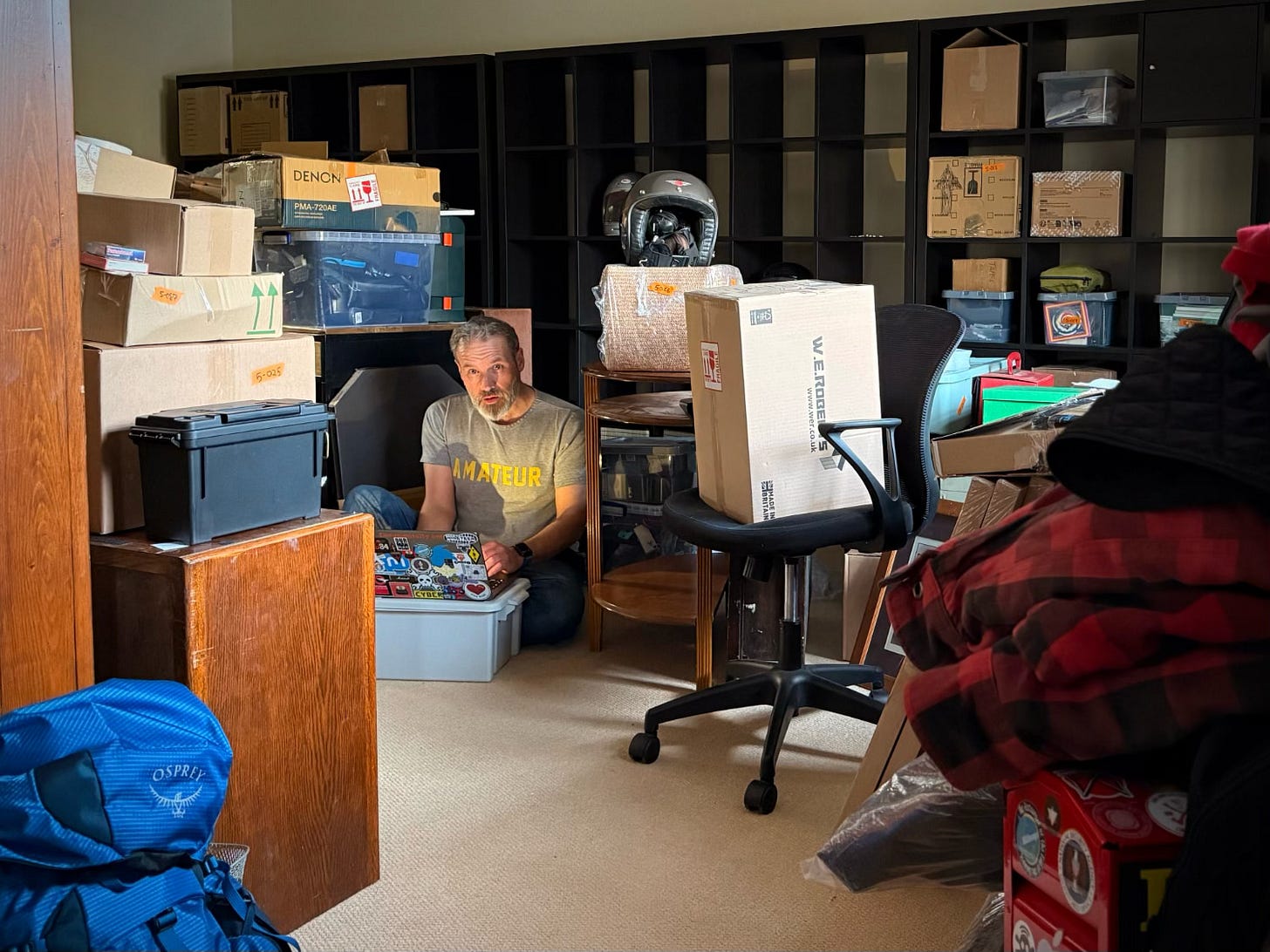 Me sat in my cluttered den surrounded by newly built shelving and lots of boxes.