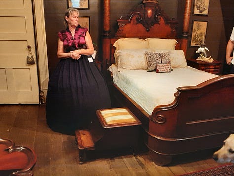 The interior of Houmas House is stately and beautiful with a wide center hall with large portraits on the wall. The second photo shows a fireplace and artwork; the third photo shows a desk in a stately room with a portrait in an ornate frame. The last photos are of bedrooms and a curving staircase.