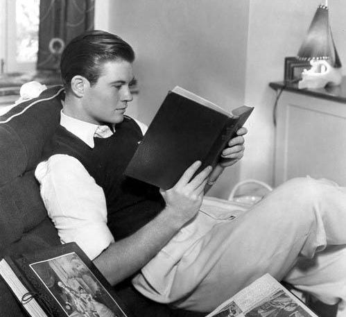 This may contain: a man sitting in a chair reading a book