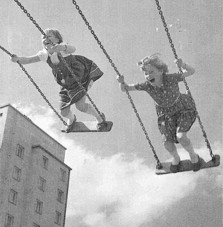 This may contain: two children on swings in the air with buildings in the back ground and clouds in the sky