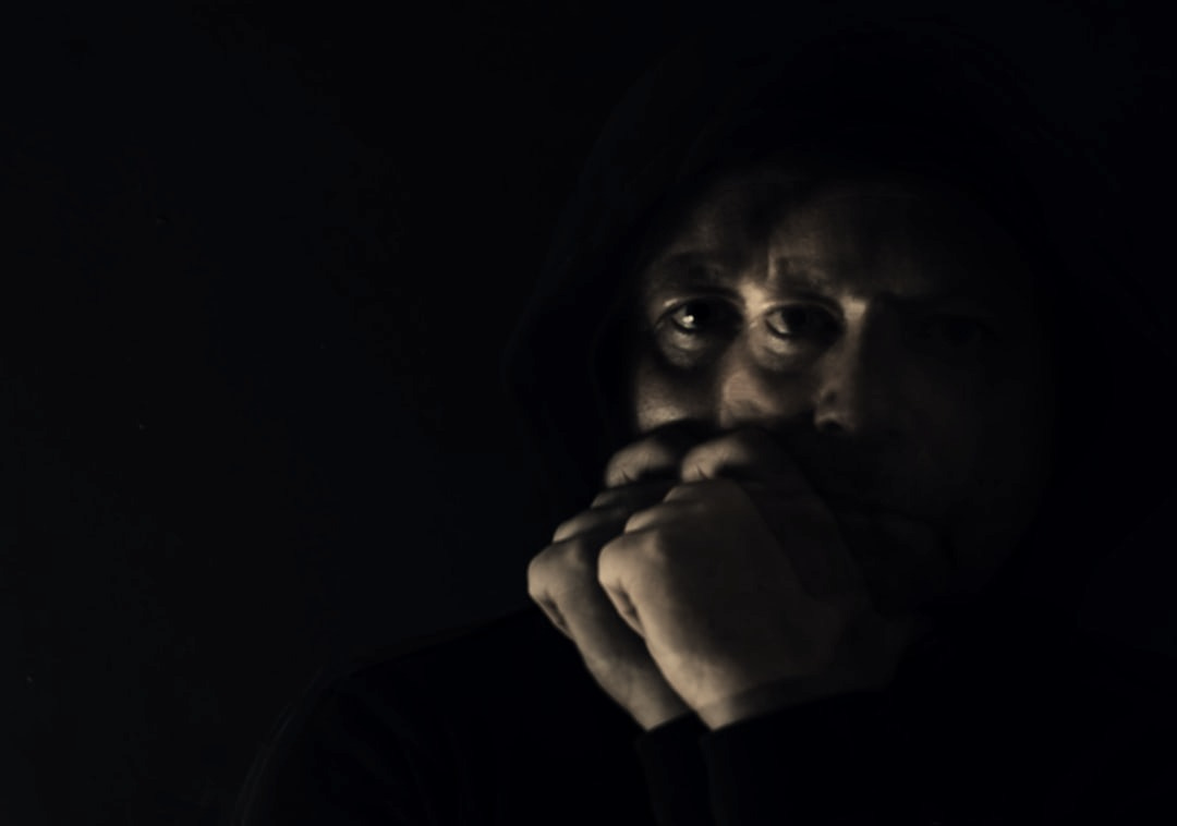 A man in a dark room with his hands on his face A man in a dark room with his hands on his face
