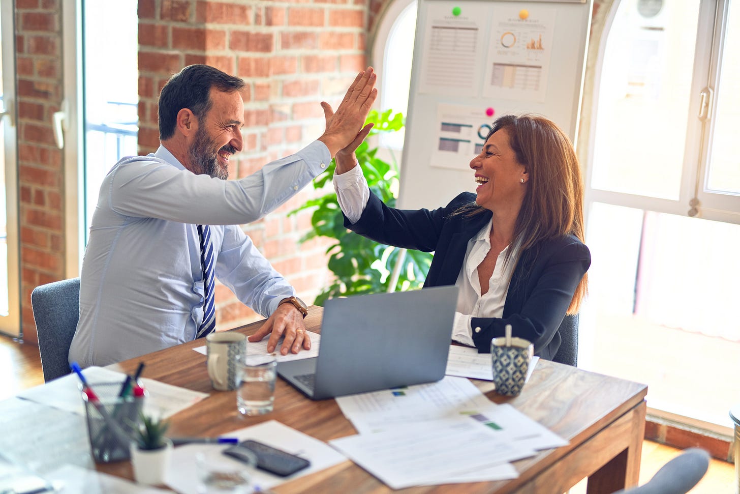 a man and a woman in business attire high-fiving in front of a laptop