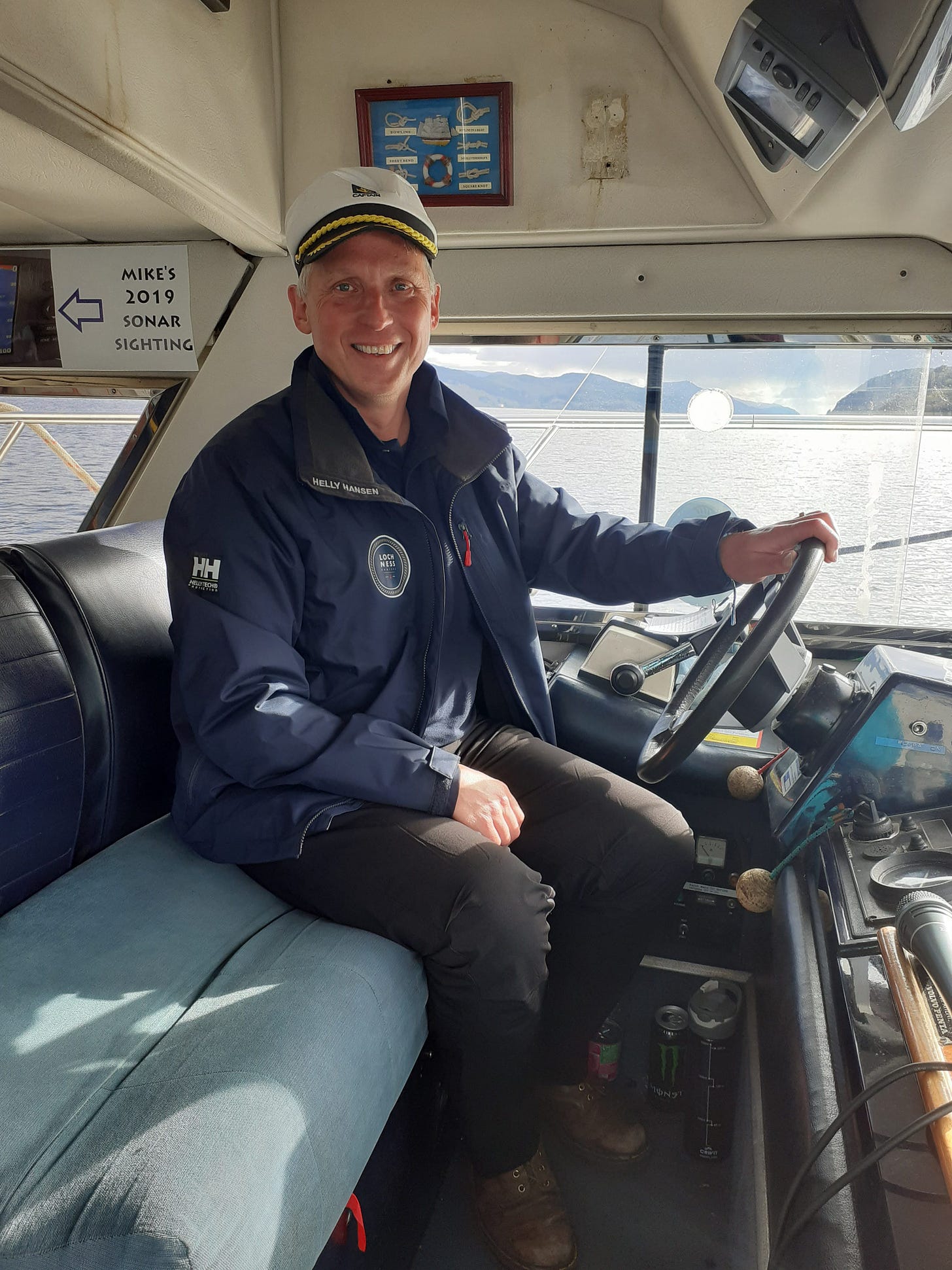 A photograph of Neil Mapes sitting in the cabin of a boat on Loch Ness, smiling and looking out over the water, representing his new part-time career as a skipper. A photograph of Neil Mapes sitting in the cabin of a boat on Loch Ness, smiling and looking out over the water, representing his new part-time career as a skipper.
