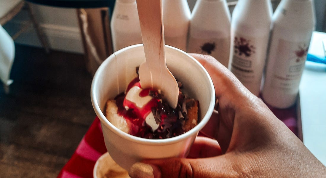 A hand holding a pot of cake with cream and raspberry sauce A hand holding a pot of cake with cream and raspberry sauce