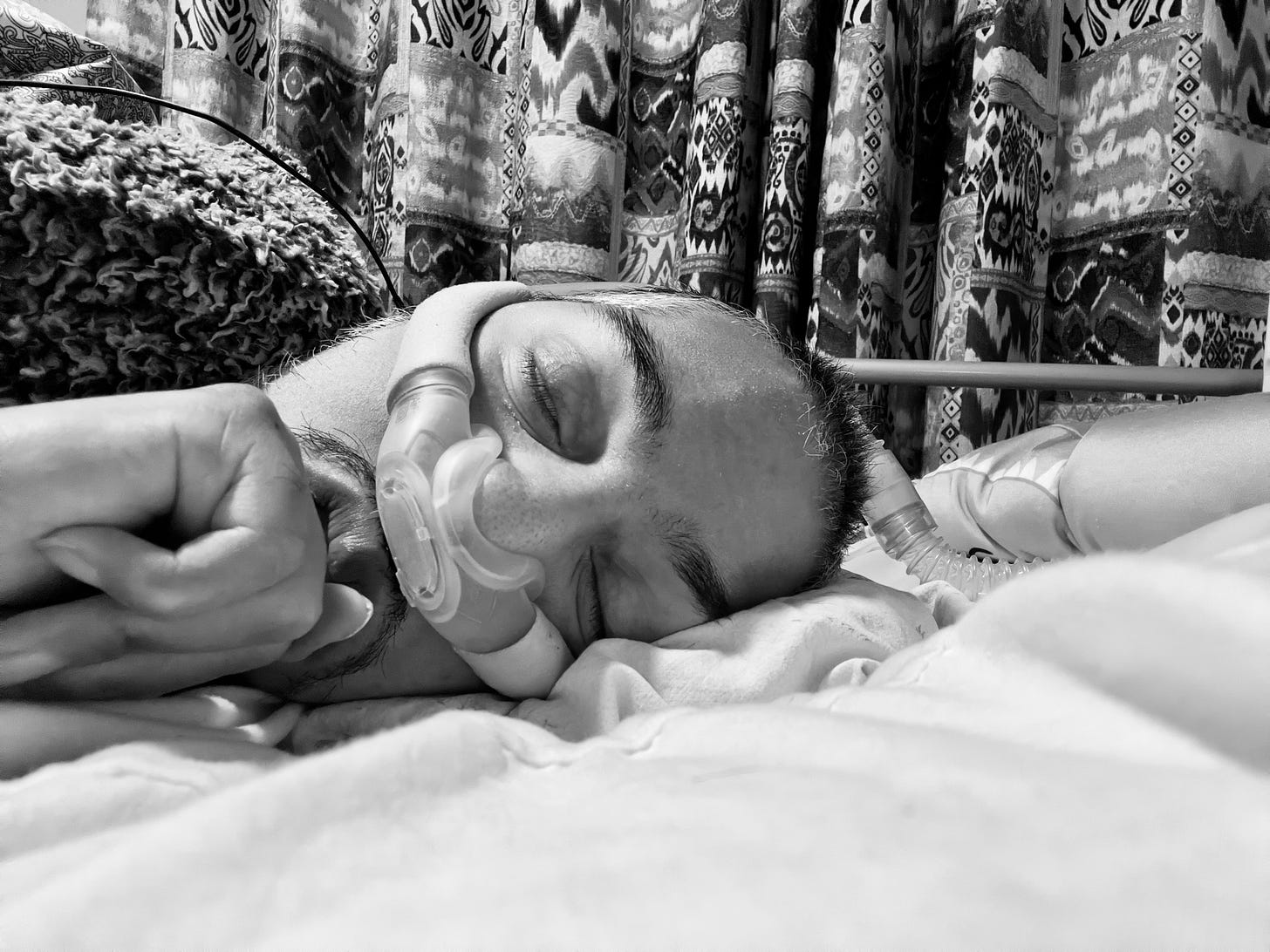 Black and white photo of Sulaiman tucked cosy under his blanket asleep in bed. He had a ventilator mask over his nose. Black and white photo of Sulaiman tucked cosy under his blanket asleep in bed. He had a ventilator mask over his nose.