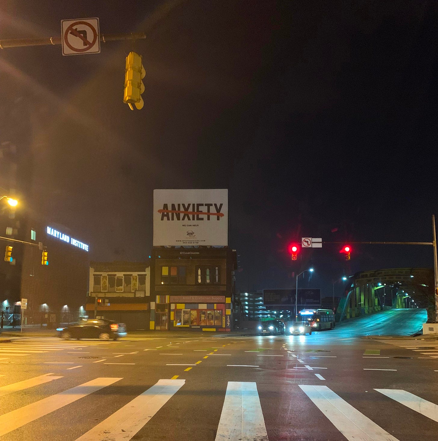 A Baltimore street corner with the Maryland Institute College of Art on one side and a billboard that says "Anxiety" in the center (crossed out) and a bridge to the right