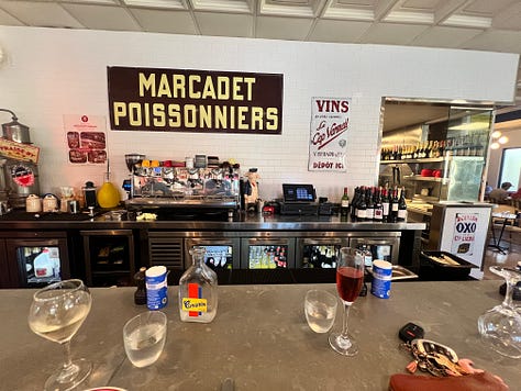 Three photos from Bouillon by Moulin: a glass of white wine and a kir royale on the counter, a decorative tile mural of a woman with a hand mirror, and a vintage Marcadet Poissonniers sign above the bar.