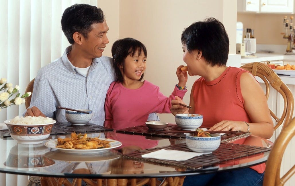 a man, woman and child sitting at a table eating food