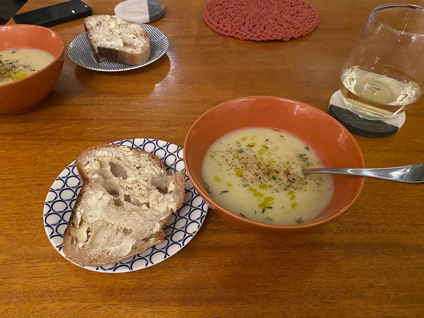 Two bowls of potato soup garnished with thyme, ground pepper, and a drizzle of olive oil. Side plates with buttered, crusty sourdough are next to the bowls.