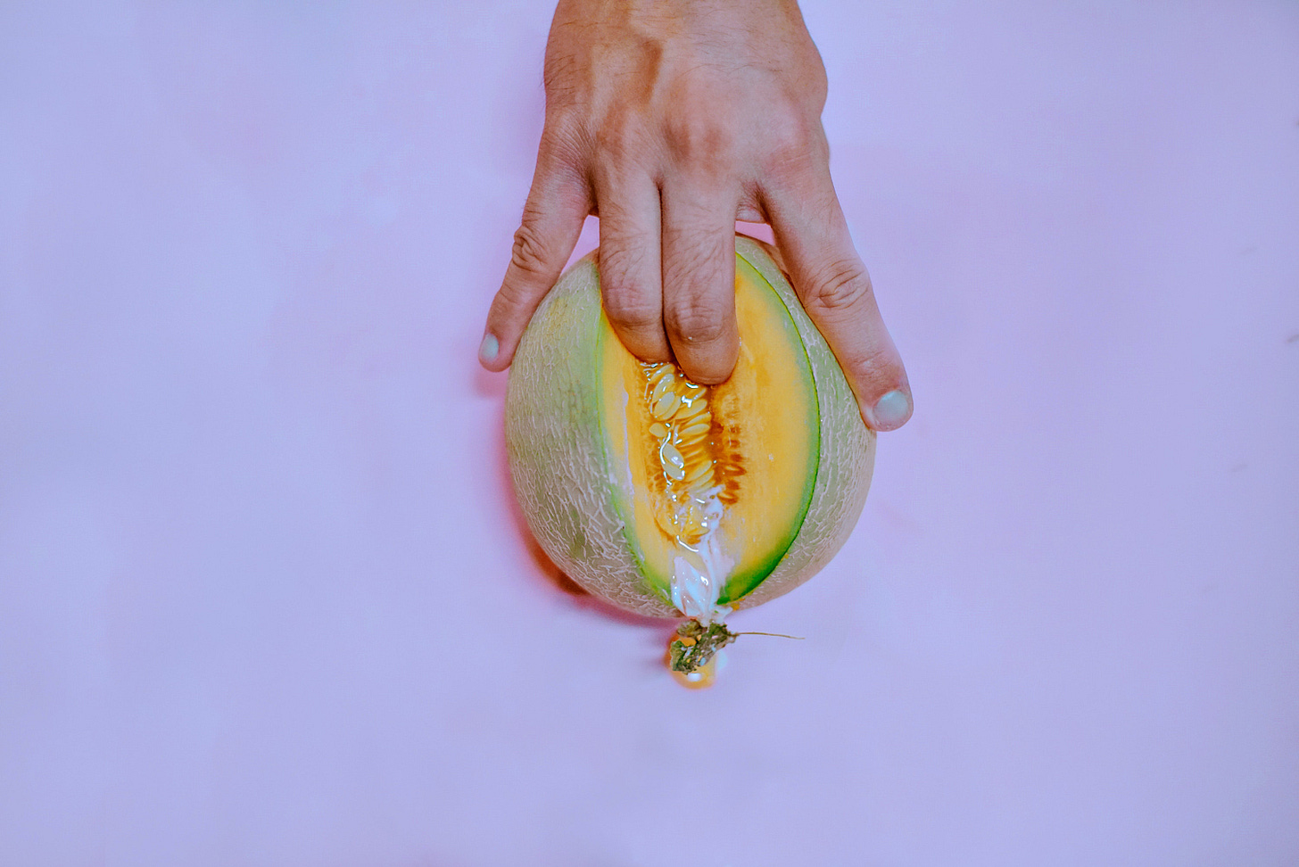 a hand, fingering a mellon, that is sliced, using the two middle fingers