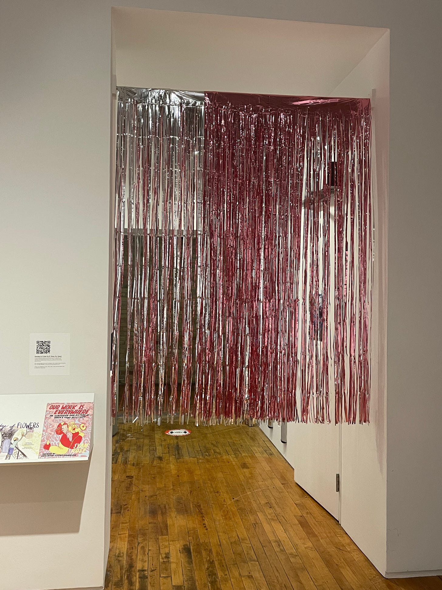 photo of a silver and pink gradient mettalic streamer from the dollar store fringe, hung as a portal into an art gallery, it's trimmed so wheelchair users can pass through and shimmers