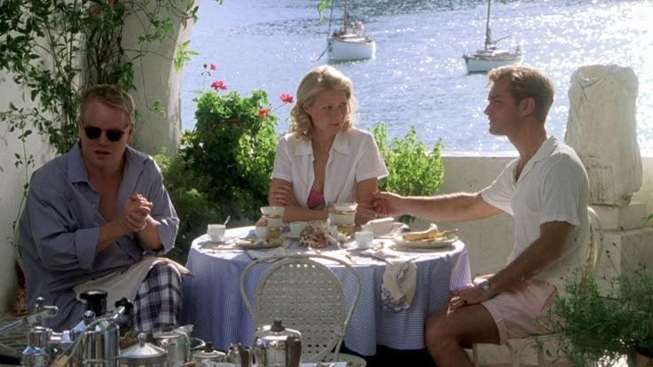 This may contain: two men and a woman sitting at a table with food in front of the water
