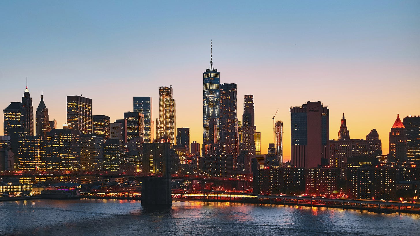 A vibrant city skyline at dusk, featuring a variety of illuminated skyscrapers with a river in the foreground and a bridge spanning across. The sky is a gradient of warm oranges transitioning into a cool blue. A vibrant city skyline at dusk, featuring a variety of illuminated skyscrapers with a river in the foreground and a bridge spanning across. The sky is a gradient of warm oranges transitioning into a cool blue.