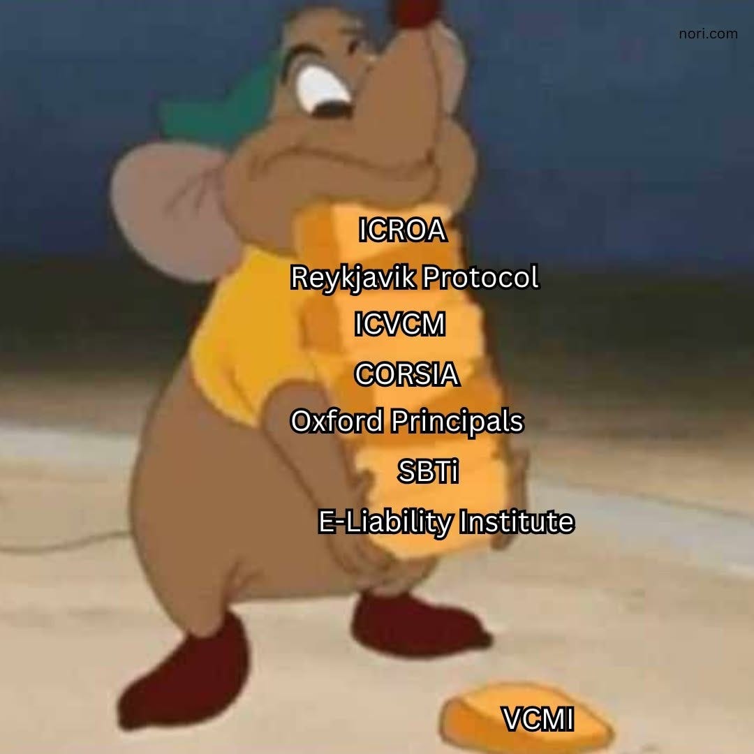 Gus the mouse from Cinderella clutching a stack of corn kernels labelled ICROA, Reykjavik Protocol, ICVCM, CORSIA, Oxford Principles, SBTi and E-Liability Institute, with one dropped kernel labelled VCMI.