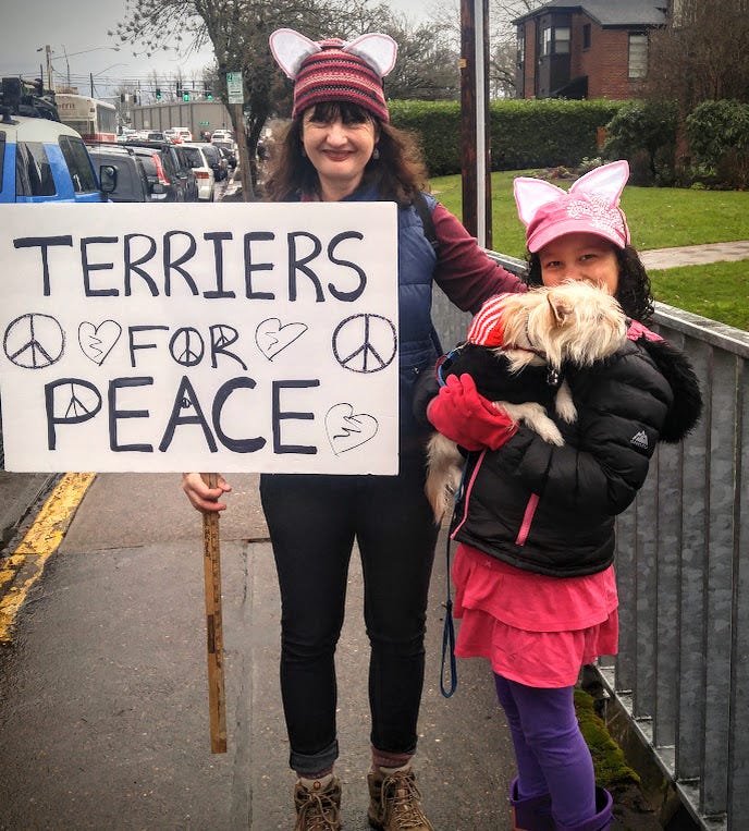 Woman with cat ears on her red striped hat and girl holding terrier, and woman is holding sign that reads Terriers for Peace.