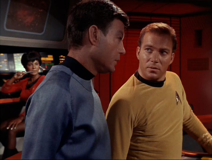 Nichelle Nichols as Uhura chews on the end of her stylus while Kirk and McCoy discuss the situation.