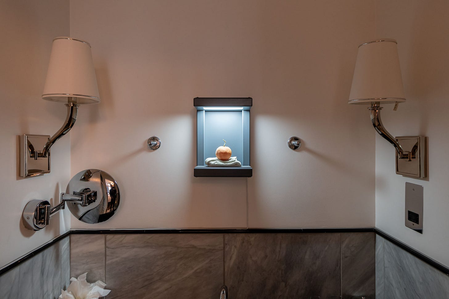 Bathroom installation view with a small lit display niche between two wall lamps, turning an everyday space into a micro-gallery.