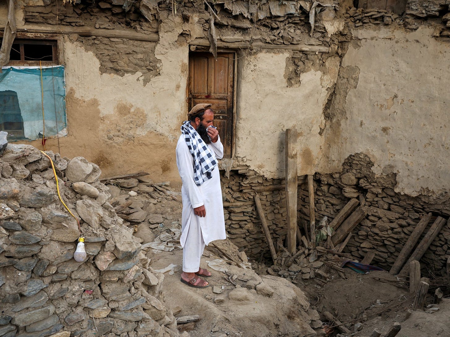 Man standing amid ruins of damaged Afghan building after the September 2025 earthquake