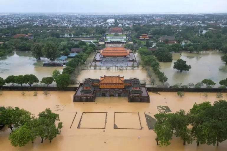 Aerial view of severe flooding in central Vietnam. Historic temples and surrounding neighborhoods are submerged under brown floodwater, with trees and structures partially underwater.