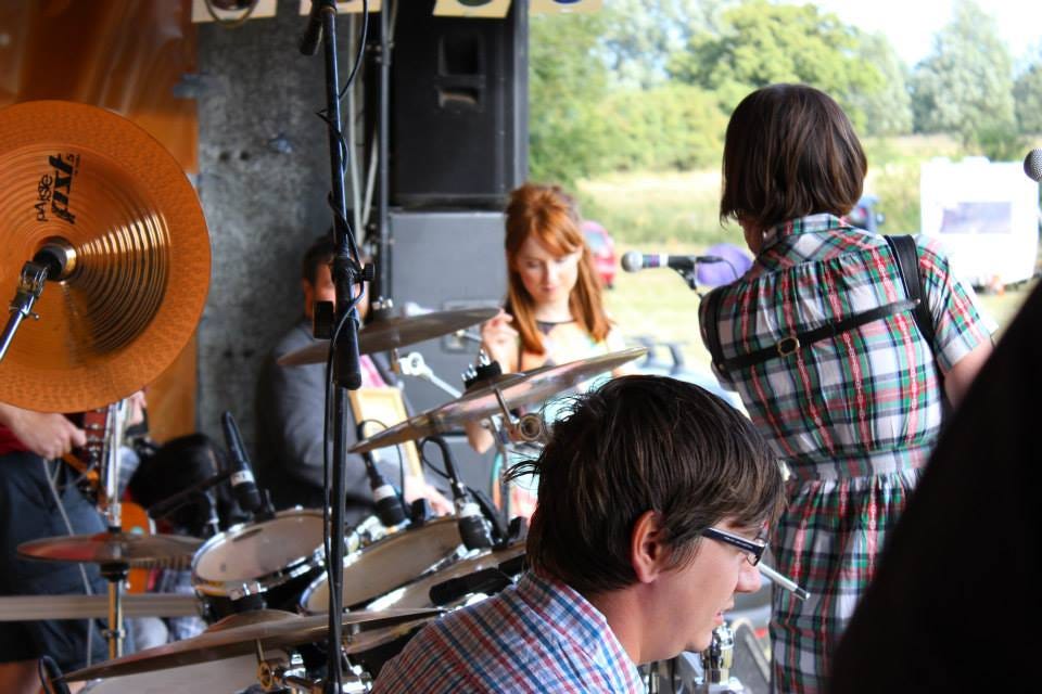Back view of musicians/singer in a band. Can't see their faces. Can see drum kit
