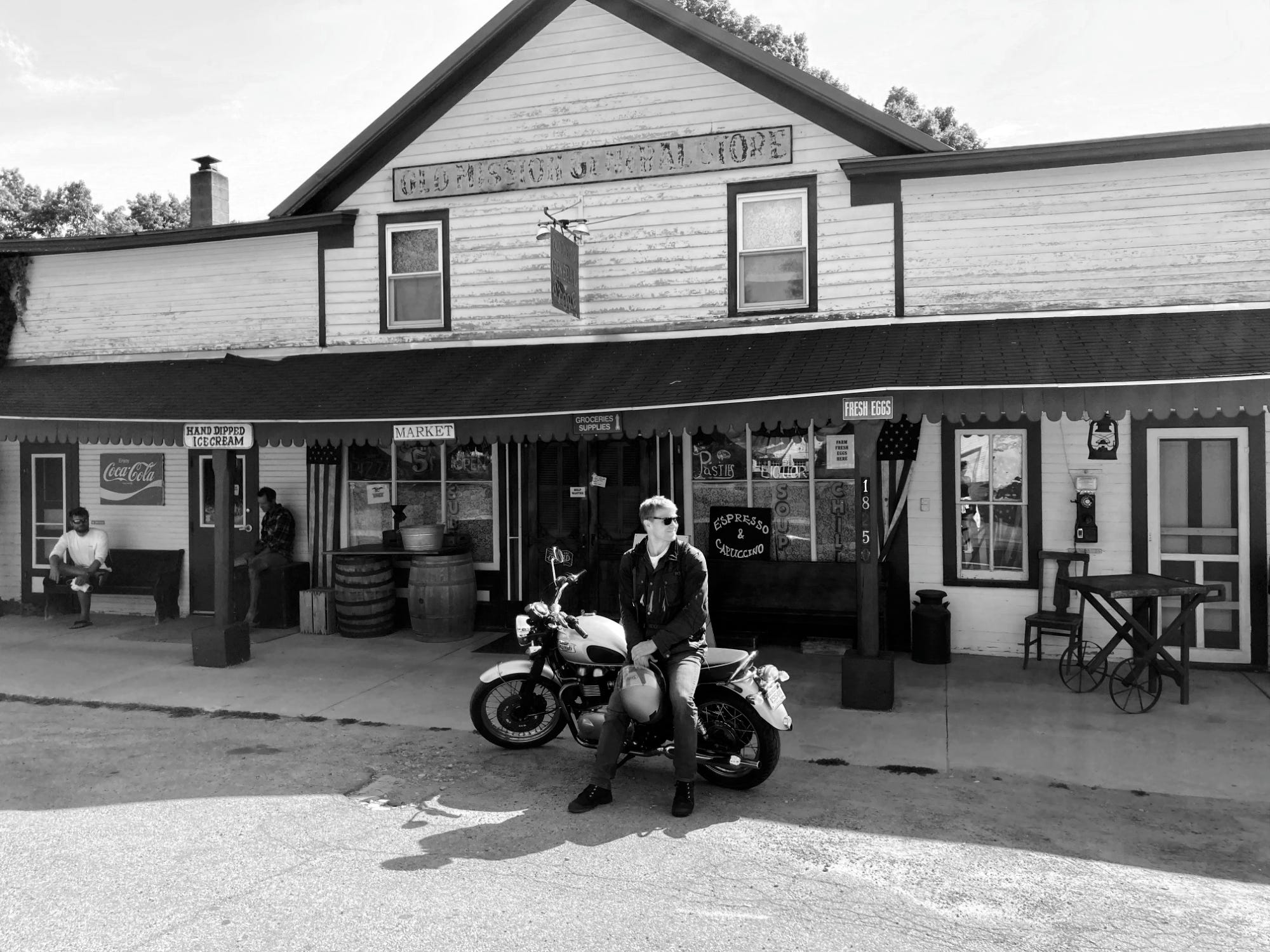 Young man leaning on a motorcycle in front of an old general store. Young man leaning on a motorcycle in front of an old general store.