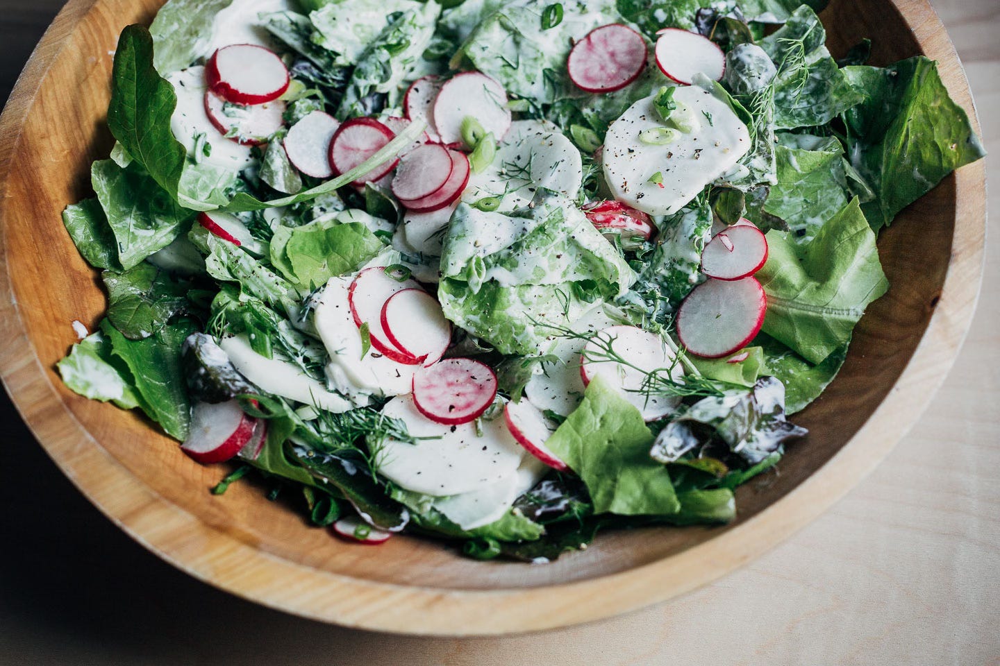 A wooden bowl with a green salad dressing with ranch dressing. 