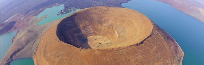 Une île circulaire et brune au milieu d'une étendue d'eau turquoise