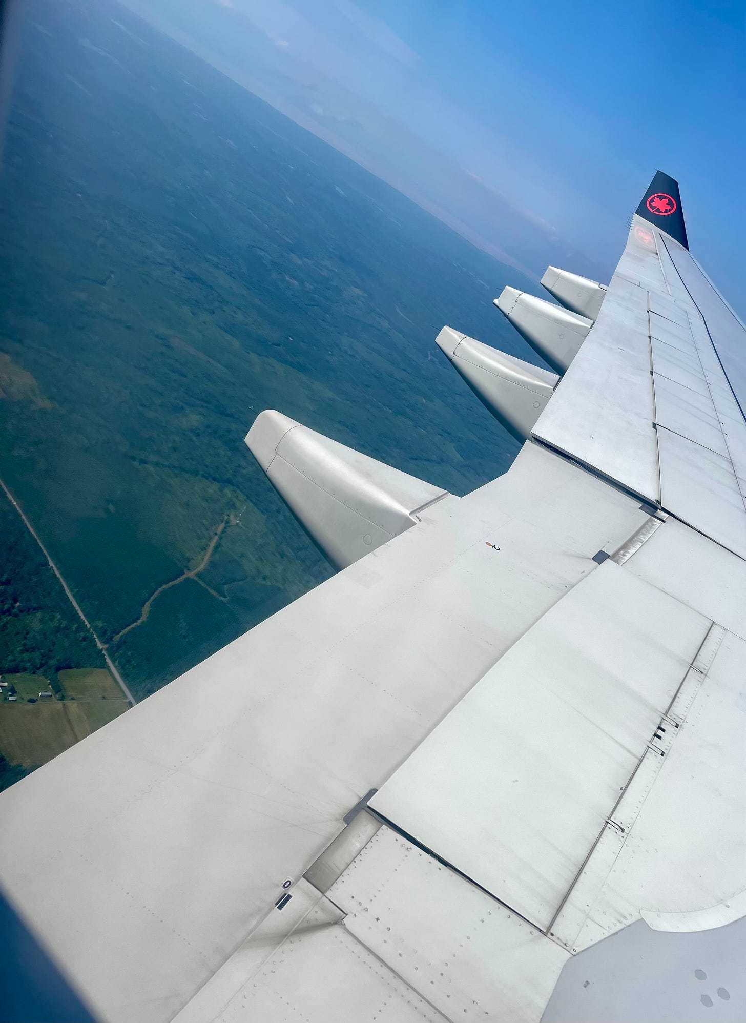 Air Canada wing through an airplane window overlooking green earth and a bit of sky