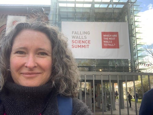 Smiling woman standing in front of building bearing a banner for the Falling Walls Science Summit