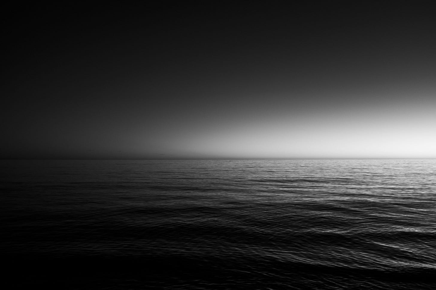 A black and white photo of a body of water at night. A black and white photo of a body of water at night.