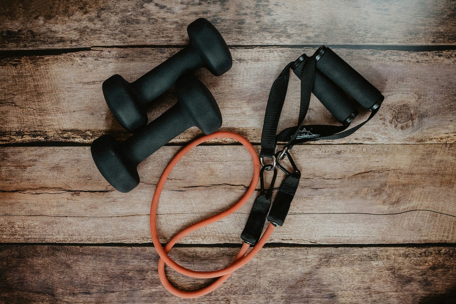 Two free weights and a resistance band on a wood background.