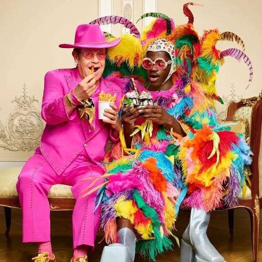 Elton John and Lil Nas X wearing each other's costumes and eating French fries and ice cream