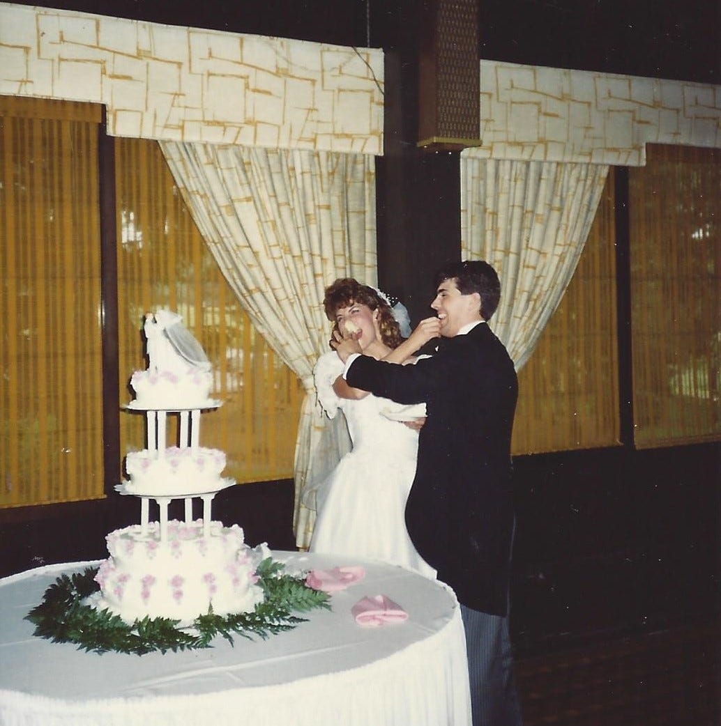 Groom smashes wedding cake into the bride's face while the bride attempts to nicely feed the groom