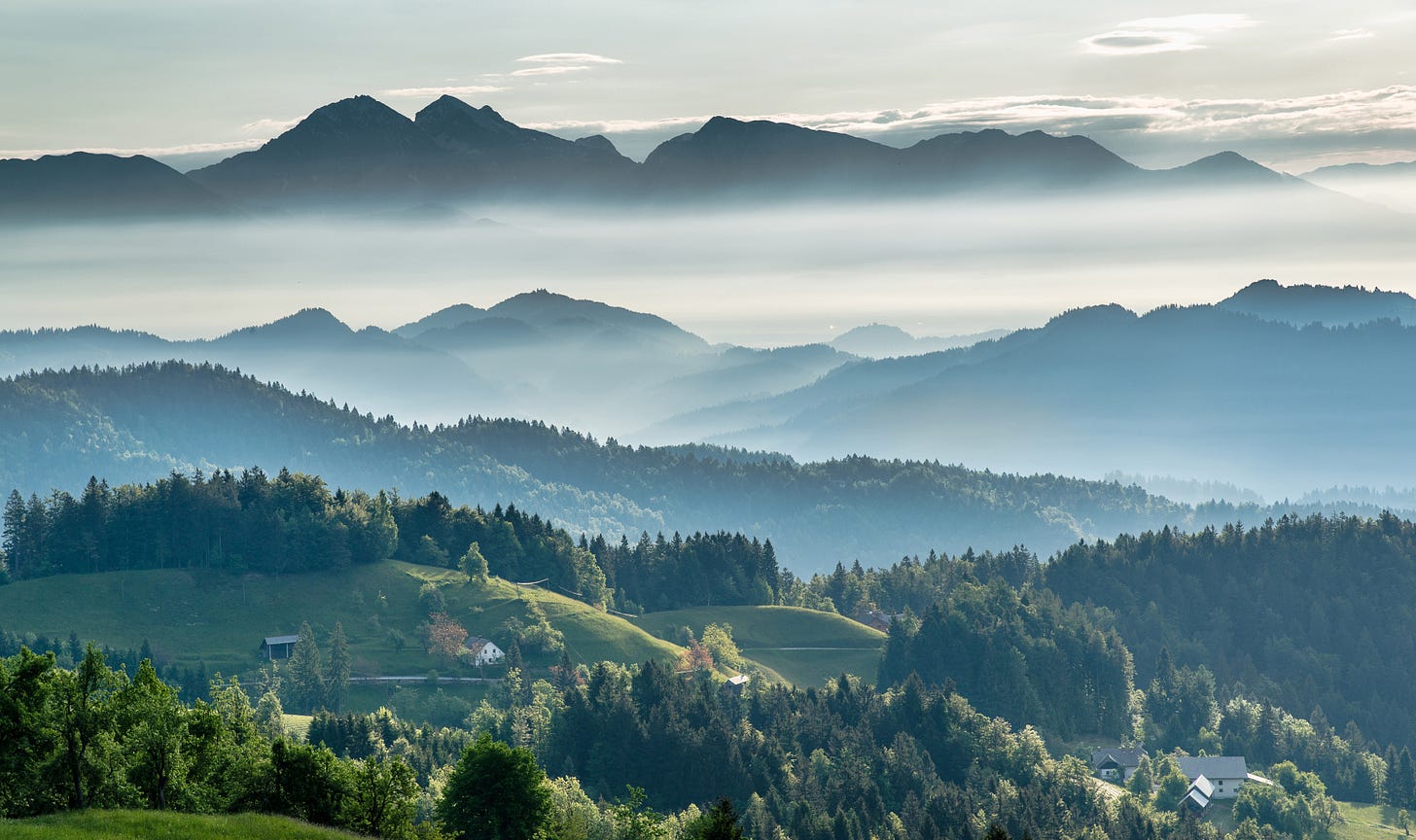 Green rolling hills with mist rolling over mountains in the background.