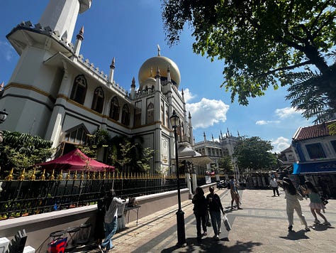 Top left photo is a green street sign that reads Haji Lane. Middle top photo is a white and blue shopping bag with Loka Made in print letters. Top right photo is a crowded street with shops on both sides of the lane. Bottom left photo is a street mural on Muscat Street. Bottom middle photo is of the Sultan Mosque. Bottom right photo is a gray mailbox and a stack of postcards being fed into the open slot. 