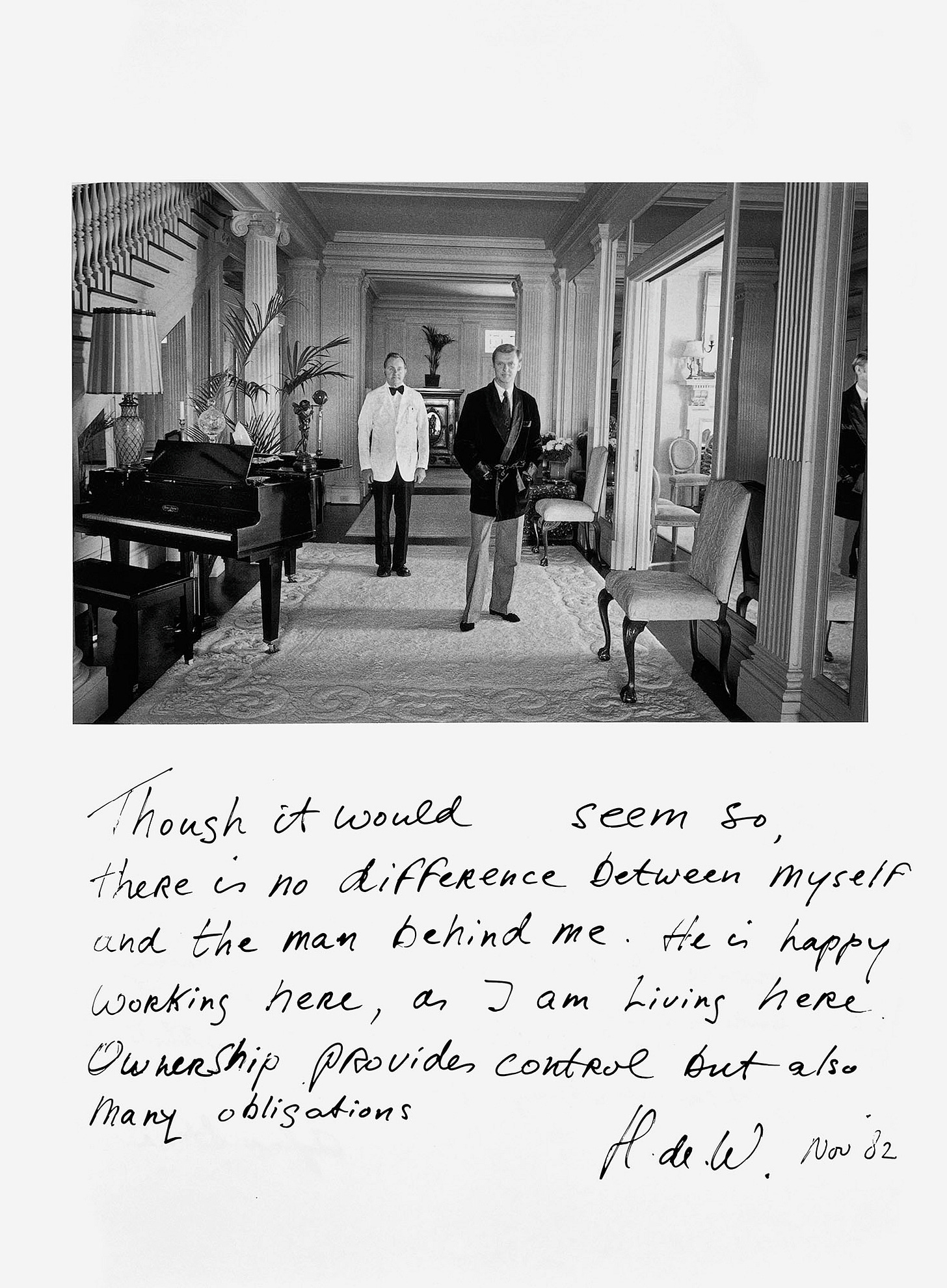 A man wearing a tie, slacks, and a robe stands with his hands in his pockets in a luxurious hall. Behind him, a man dressed in a formal white uniform waits attentively. The handwritten caption says, "Though it would seem so, there is no difference between myself and the man behind me. He is happy working here, as I am living here. Ownership provides control but also many obligations. —H. de W. Nov ‘82"