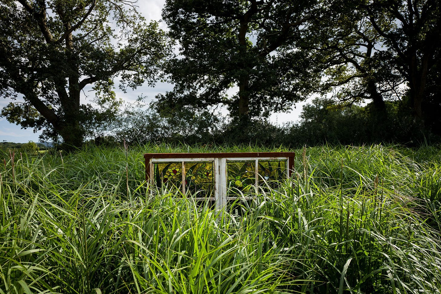 A stained glass window sits in amongst tall grass on a sunny day.