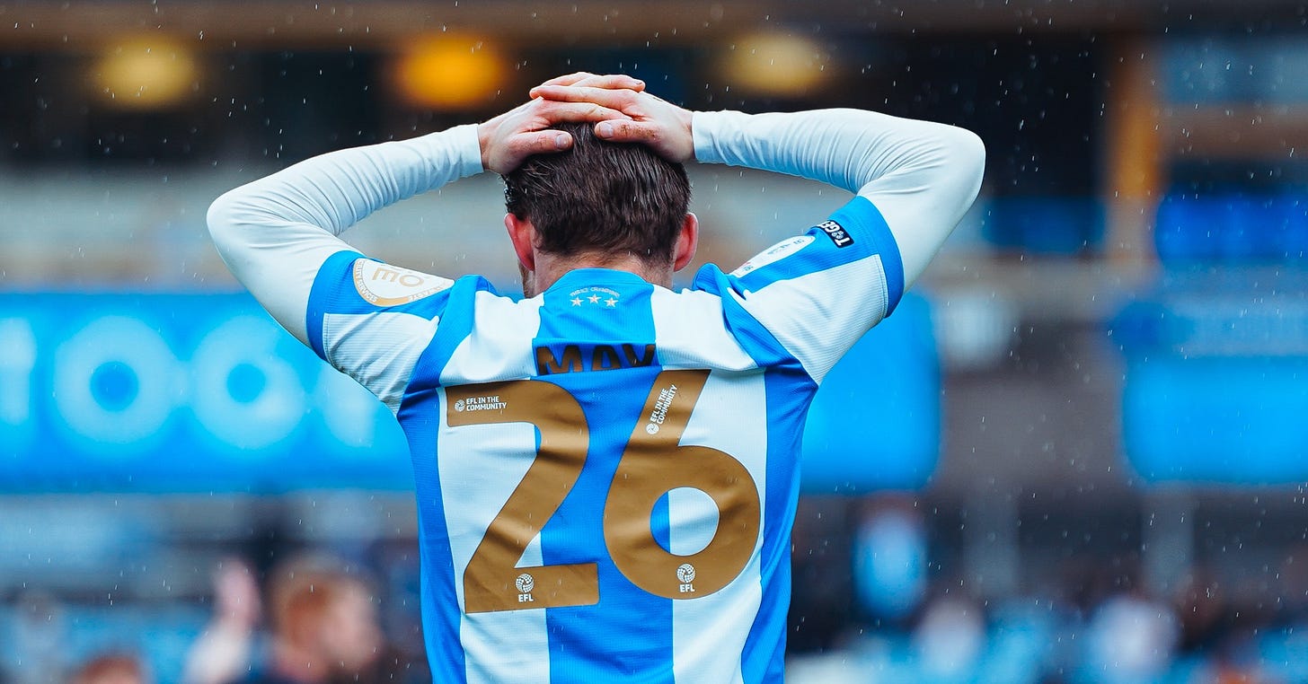 Huddersfield Town player Alfie May, facing away from the camera, puts his hands on his head, with the Accu Stadium in the background. Huddersfield Town player Alfie May, facing away from the camera, puts his hands on his head, with the Accu Stadium in the background.