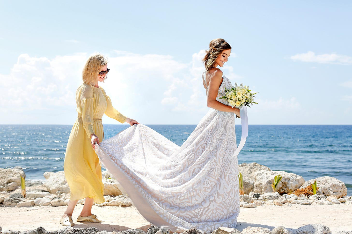 A wedding planner helps a bride with her dress. Two women by the sea at a wedding A wedding planner helps a bride with her dress. Two women by the sea at a wedding