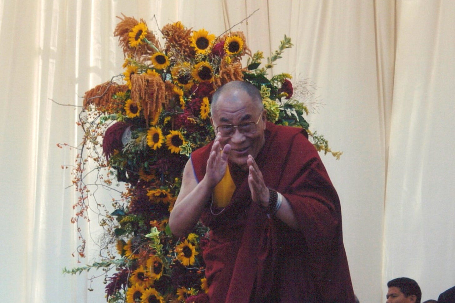 The Dalai Lama waving in front of huge bunch of sunflowers