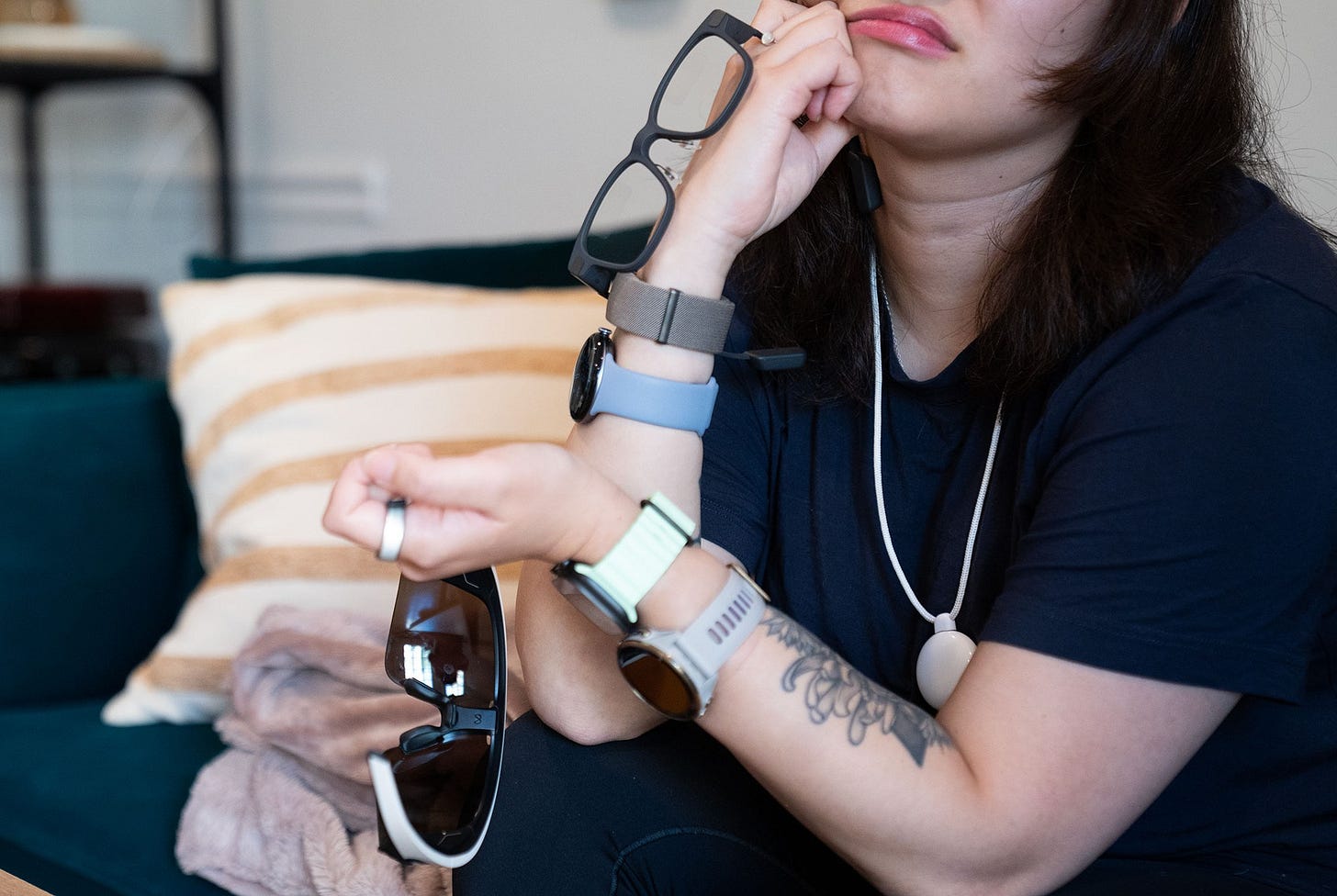 Close up of Senior Reviewer Victoria Song pondering her life choices while holding two smart glasses, four wrist-based wearables, a smart ring, and the Friend AI necklace.