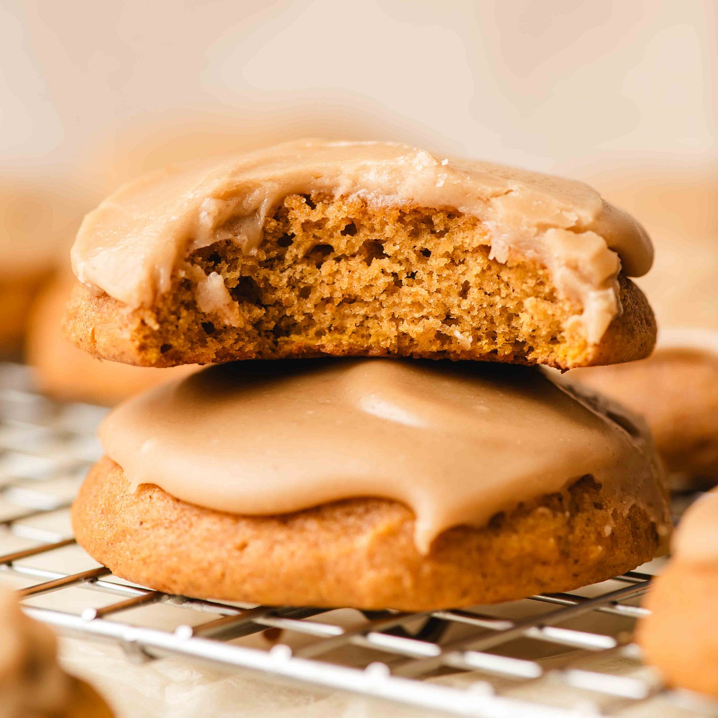 Stack of frosted pumpkin cookies with a bite taken out of the top one.
