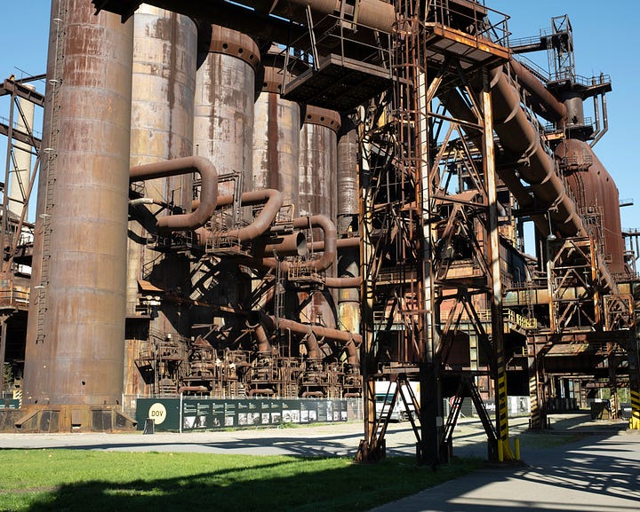 Colour photographs of decaying old steel factory; lots of rust pipes, stacks, and other industrial architecture