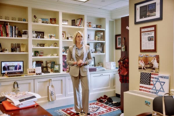 A woman stands posing for a portrait in front of a bookshelf in an office