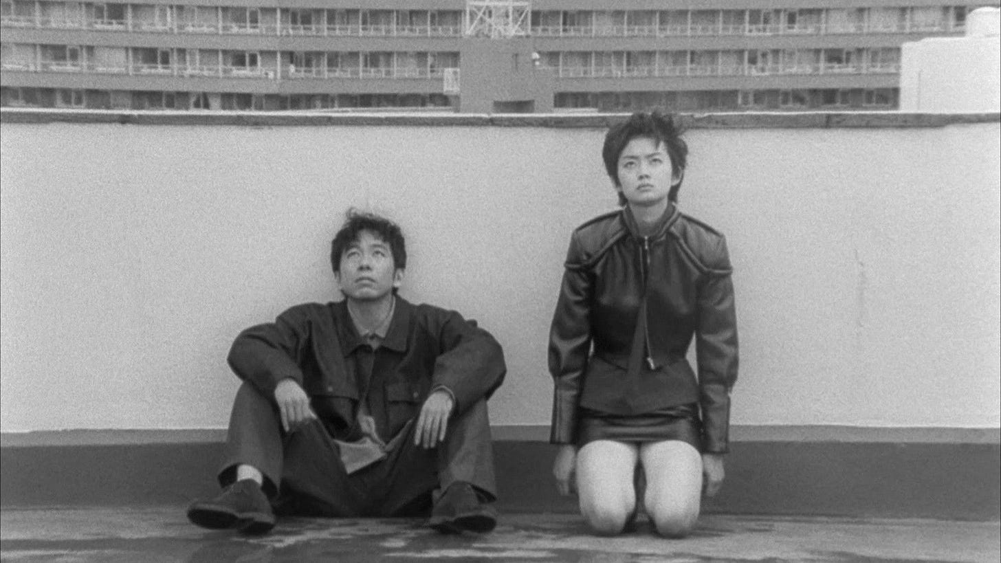 Bullet Ballet | Still features two people sitting against a rooftop. Bullet Ballet | Still features two people sitting against a rooftop.