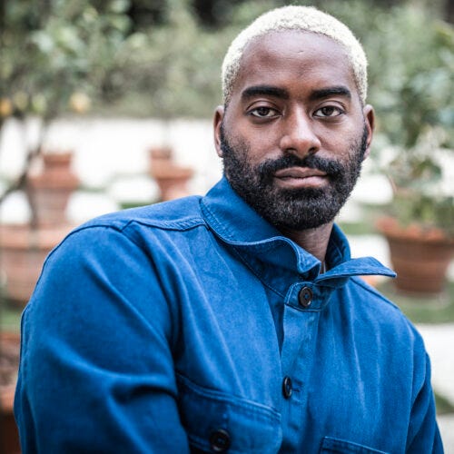 A dark-skinned Black man with a beard and blonde hair stands wearing a bright-blue worker jacket in front of a garden. A thin Taiwanese femme with bleach blonde hair and black wing eyeliner sits on their fire escape surrounded by basil leaves in their garden.